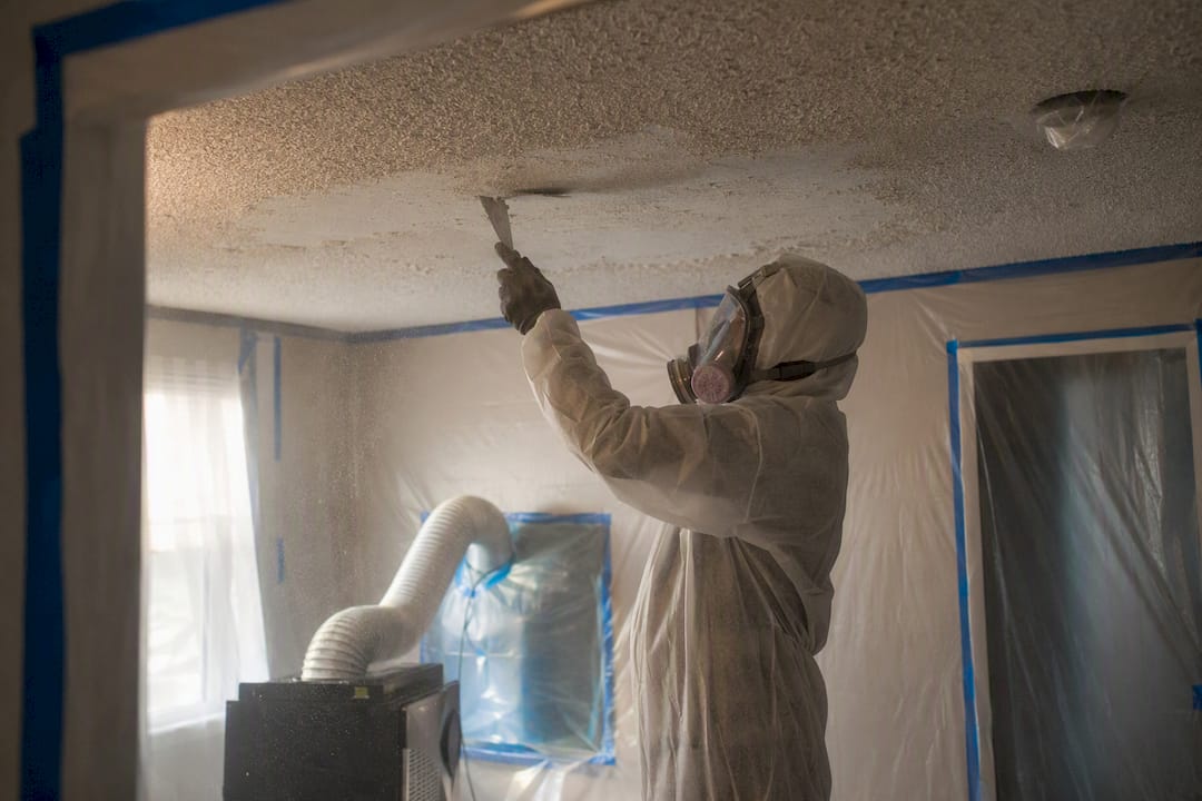 Technician removing hazardous ceiling material indoors